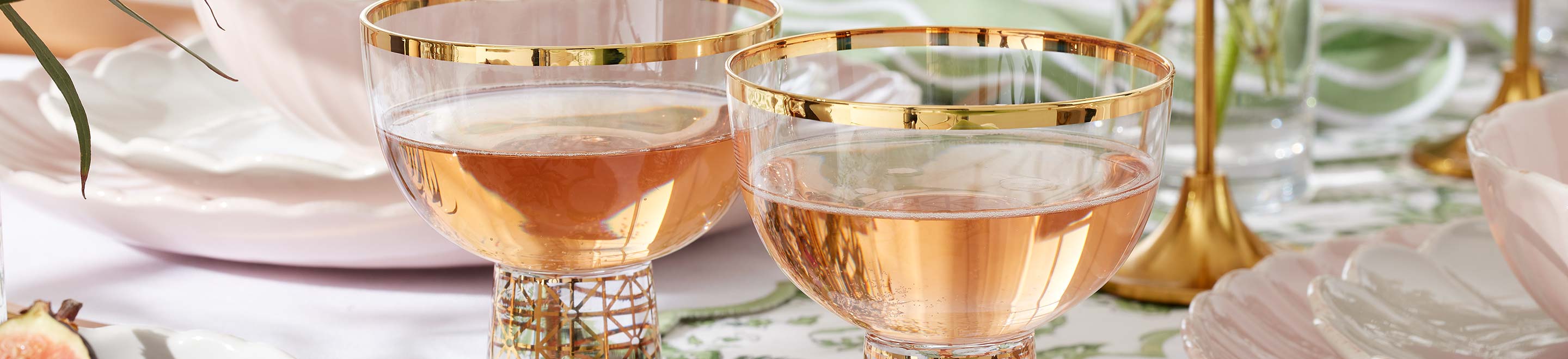 A cocktail glass filled with a golden beverage served with a sugar rim and cinnamon stick paired with an apple as decoration on the table.