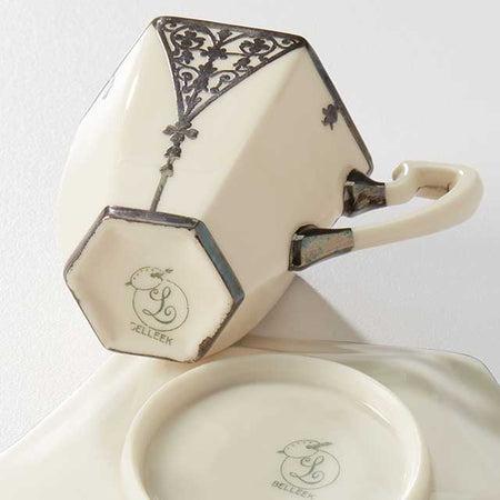 Cream-colored ceramic teacup with silver decorative detailing and matching saucer.