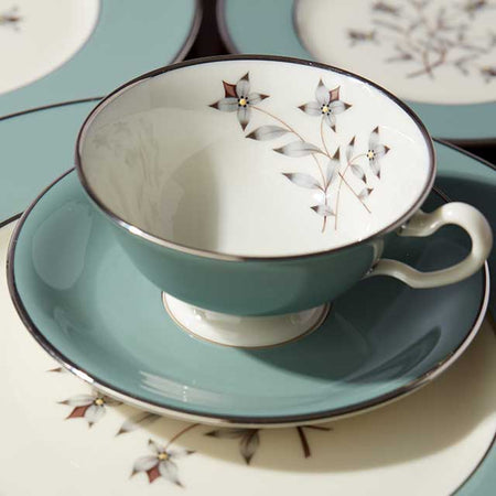 Teal ceramic teacup and saucer with a delicate floral motif and silver trim.