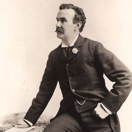 Vintage sepia-toned portrait of a man with a mustache, dressed in a dark three-piece suit with a lapel flower.