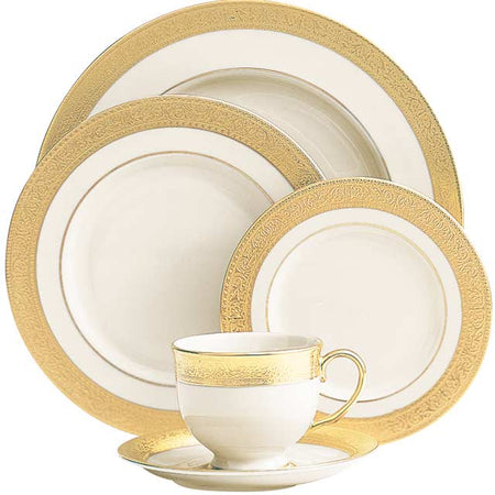 Formal cream porcelain dinnerware set with wide, ornate gold borders including plates, a teacup, and a saucer.