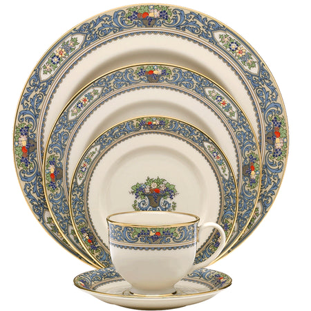 Cream porcelain dinnerware set with ornate blue scrollwork borders and fruit basket motifs, featuring plates, a teacup, and a saucer.