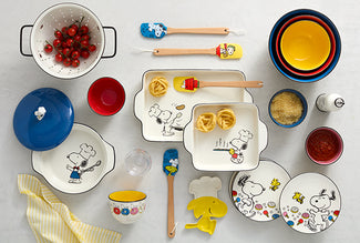 Assortment of Snoopy-themed kitchenware and baking dishes with colorful spatulas on a light marble surface.