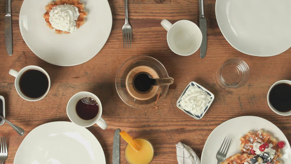 Wooden table set with waffles, coffee, whipped cream, and orange juice.
